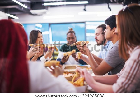 Friendly diverse multiethnic business team eating sharing pizza together in startup office, multiracial coworkers staff group enjoying break talking laughing on lunch time at meeting