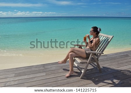 Beautiful young woman in bikini lying on a deckchair with a drink by the sea