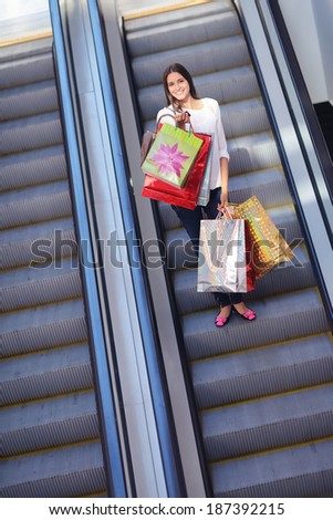 Happy young woman on scalators in a shopping mall with colorful fashion gift  bags
