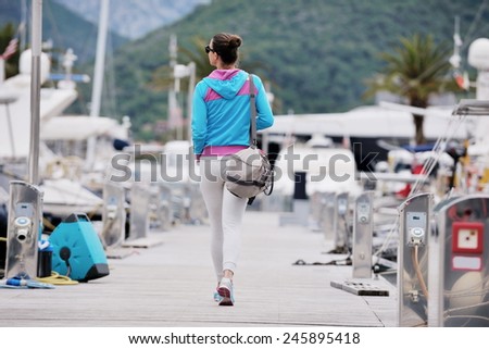 relaxed young woman walking in marina with yacht boats in background