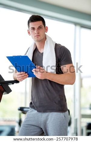 Portrait of a smiling male trainer with clipboard standing in a bright gym