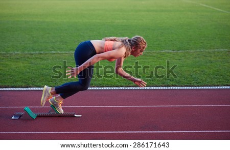 woman  sprinter leaving starting blocks on the athletic  track. Side view. exploding start