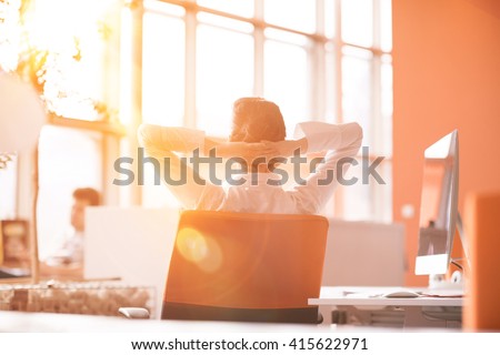 Happy young business woman relaxing and geting insiration while working on desktop computer at modern bright  starup office interior. Morning sunrise or sunset with sun flare in background.