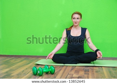 pretty girl practicing yoga in fitness club with green wall in background