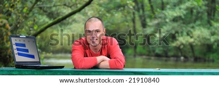 one young businessman working on laptop outdoor with green nature in background and stock progress graph on display