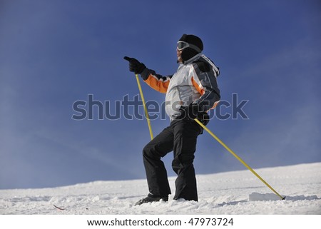 young skier relaxing, with hand pointing and  looking mountain range at beautiful sunny winter day