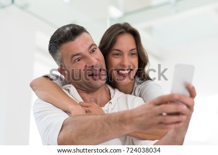 Young happy couple using mobile phone at home together, looking at screen, smiling.