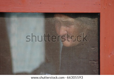 SANCRAIU, ROMANIA - DECEMBER 7: An old widow watches the traditional Winter Chase Away procession in the village,  from behind her mosquito net , on December 7, 2008 in Sancraiu, Romania