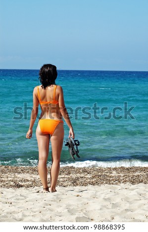 A sexy woman standing in front of the sea in orange bikini and flip-flops