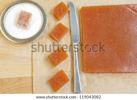 Cut off pieces of homemade marmalade on baking paper on a wooden table next to a plate of sugar