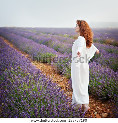 Red-haired white woman in a long white shirt on a lavender field, his back, his arms outstretched