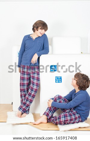 Two European boy in pajamas, one stands on the stove, the second sitting and looking at the first