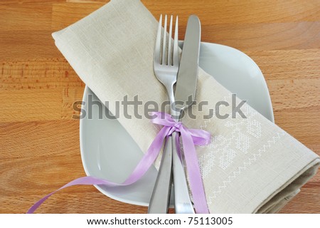 White plate, fork and knife, tied with purple ribbon, with a linen cloth on a wooden table