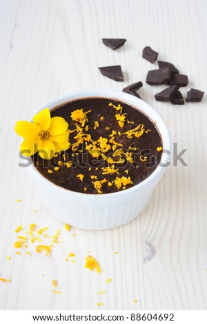 chocolate mousse, sprinkled with orange zest and decorated with a yellow flower on a wooden table, near the spill zest and slices of chocolate, vertical frame