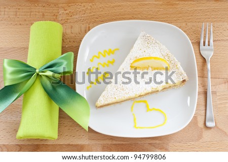 lemon cake on a white porcelain plate, dessert fork and a napkin tied with a bow green, wooden table