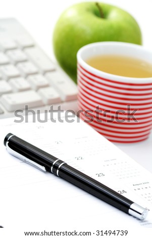 quick lunch in the office - green apple and cup of tea /focus on pen/