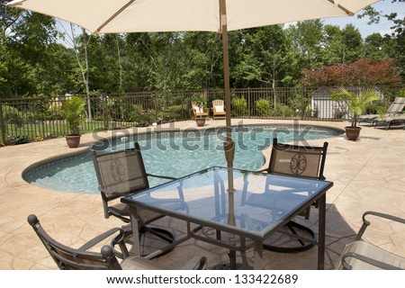 A view of a luxury salt water pool and patio in a residential backyard through patio furniture.