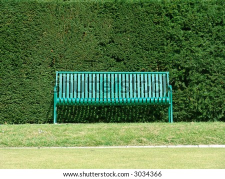 Green bench with hedge behind