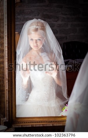 beautiful bride wearing white wedding dress under  chiffon veil in front of mirror