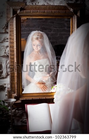 beautiful bride wearing white wedding dress under  chiffon veil in front of mirror