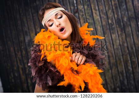 beautiful actress in brown and orange boa singing against old wooden gate