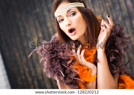 beautiful actress in brown and orange boa singing against old wooden gate