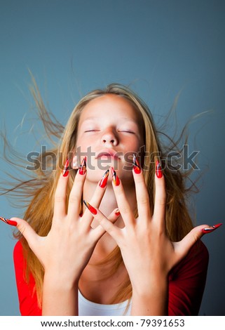 blonde girl with closed eyes and hair fluttering on wind hiding shows beautiful hands with long fingers and fashionable design of nails on dark blue background