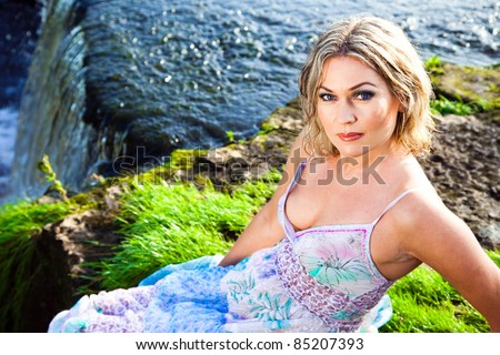 Portrait of beautiful girl enjoying beauty of nature on brink of precipice of river waterfalls in early summer morning