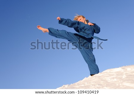 young woman in blue uniform training combat sport outdoors in winter, barefoot on the snow