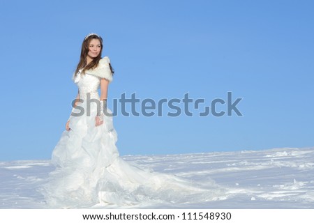 pretty young woman posing in wedding dress with train, on winter snow