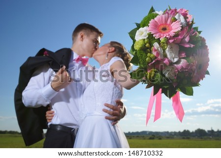 Wedding shot of bride and groom stand in field (focus on bouquet)