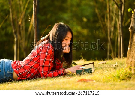 Pretty young chinese woman lie on the grass in the park and make notes in the notebook