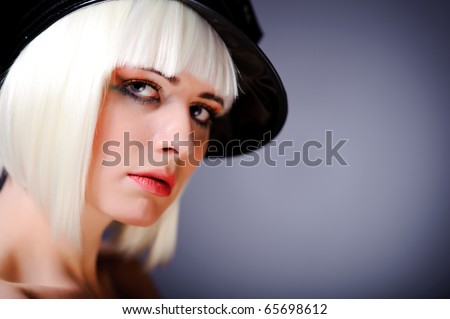portrait of model with blonde hair and black peaked cap, isolated on grey.
