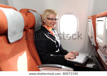 smiling businesswoman posing with laptop on the board of plane