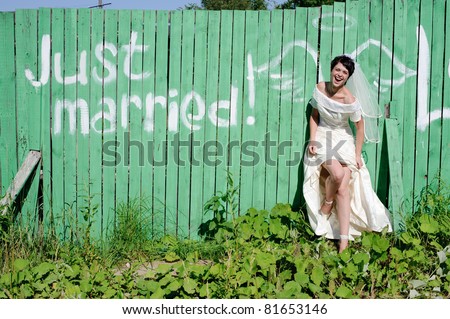 young happy bride near picture of angel wings on green fence