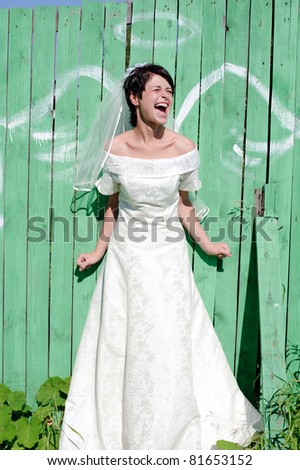 young happy bride near picture of angel wings on green fence