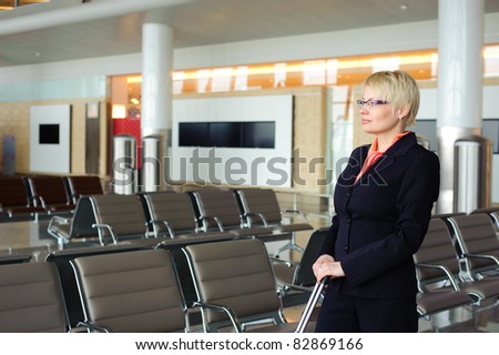blonde adult businesswoman in black suit waiting for the departure of the plane in waiting room