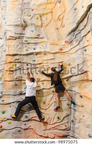 competition of young businesswoman and businessman on rock wall in sport center