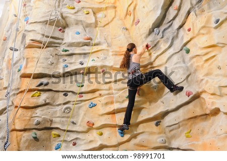 active young woman on rock wall in sport center