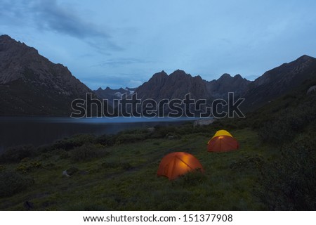 lit tents on lake shore facing mountain at evening