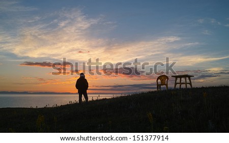 a man stands alone in lake shore waiting for sunrise