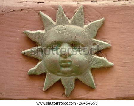An old oxidized brass shape in the form of a staring sun attached to a wooden door to ward off evil spirits