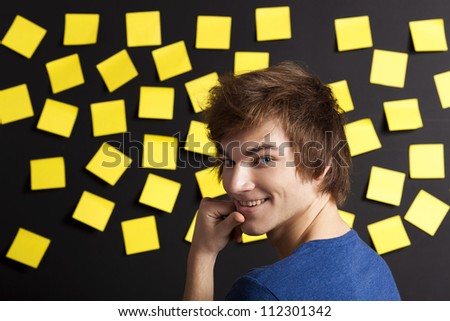 Young student in front of a board with yellow notes and looking in to the camera