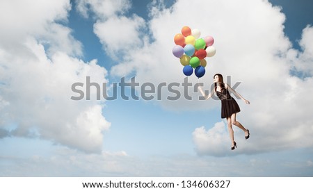 Fashion photoshoot with  a beautiful young woman flying with balloons over the sky