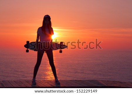 Beautiful And Fashion Young Woman Posing At Teh Sunset With A Skateboard
