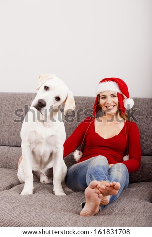 Woman sitting on the sofa with her dog and wearing a santa hat