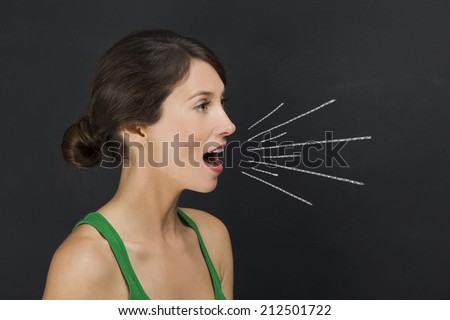 Beautiful young student giving a speech over a chalkboard with rays coming out from her mouth
