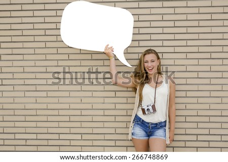 Beautiful and young teenager holding a thought balloon, in front of a brick wall