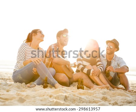 Friends having fun together at the beach, playing guitar and drinking beer