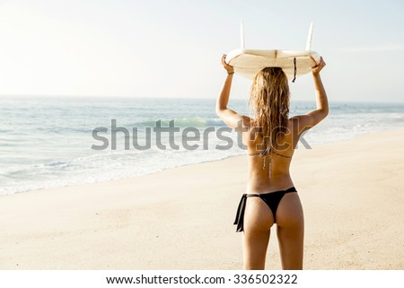 Beautiful young girl holding a surfboard and checking the waves